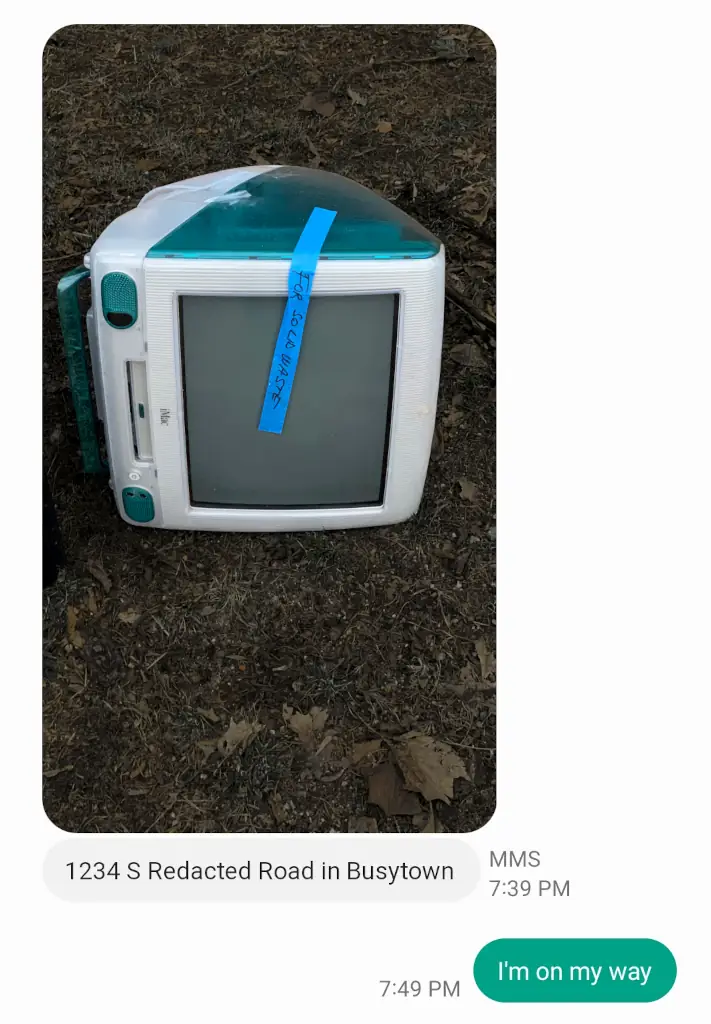 An SMS conversation.
<p>In the first message, a Bondi Blue iMac G3 (large translucent 90s all-in-one computer) lies on its side in brown grass. It has tape on it that says "for solid waste". The message also includes an address: 1234 S Redacted Road in Busytown.</p>
<p>The second message (a reply) is a simple "I'm on my way"." class="wp-image-1687" width="356" height="512"><figcaption class=