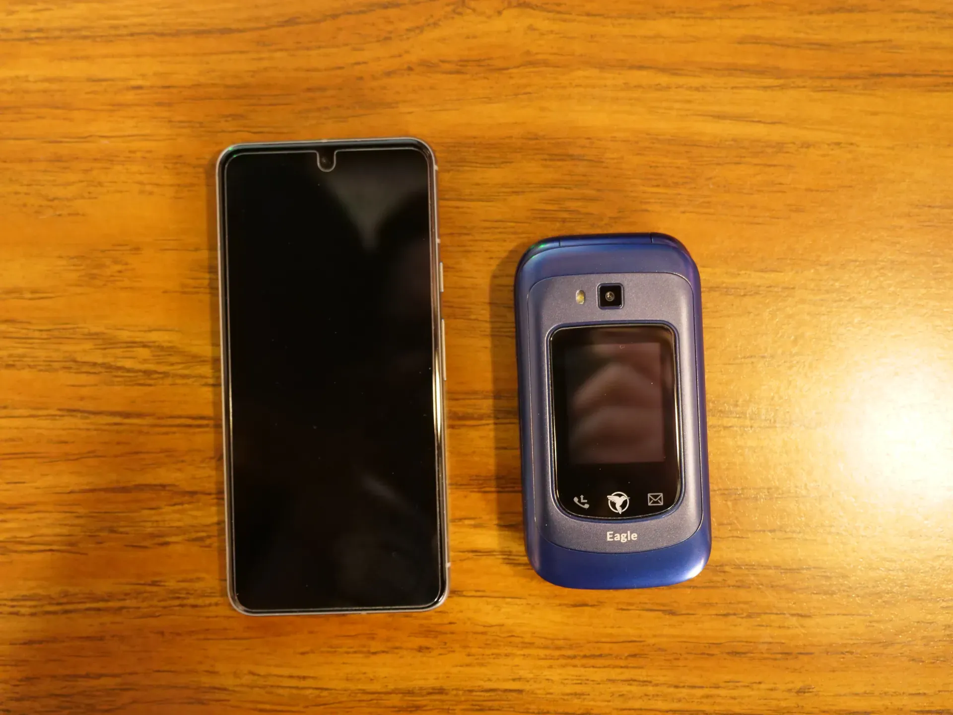 A blue dumbphone next to a modern smartphone. The dumbphone appears about 3/4 the size of the smartphone.