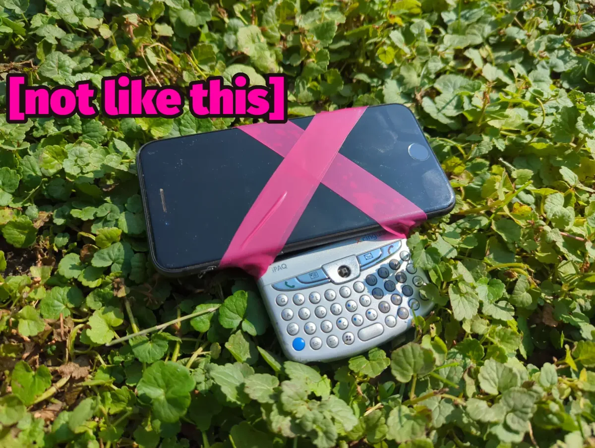 It's a smartphone taped to an older BlackBerry-style phone. The phones are sitting in a field of clover and superimposed are