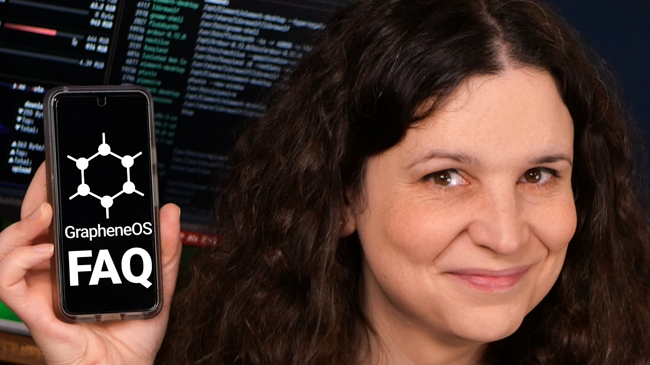 A close-up of my smiling face, holding a phone with the GrapheneOS logo on it and the word "FAQ".